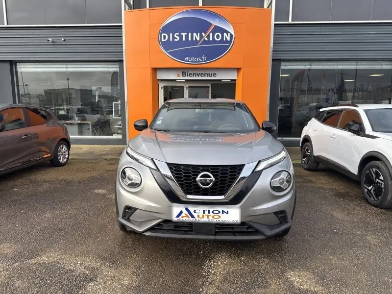 Vue de face d'un Nissan Juke gris perle métallisé garé devant une concession avec logo Distinxion visible.