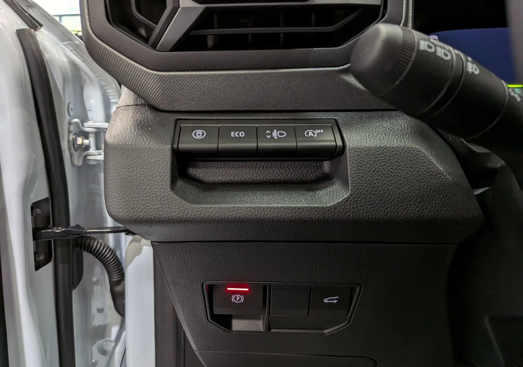 Gros plan sur les commandes à gauche du volant du Dacia Bigster blanc glacier, avec bouton de frein à main électronique allumé.