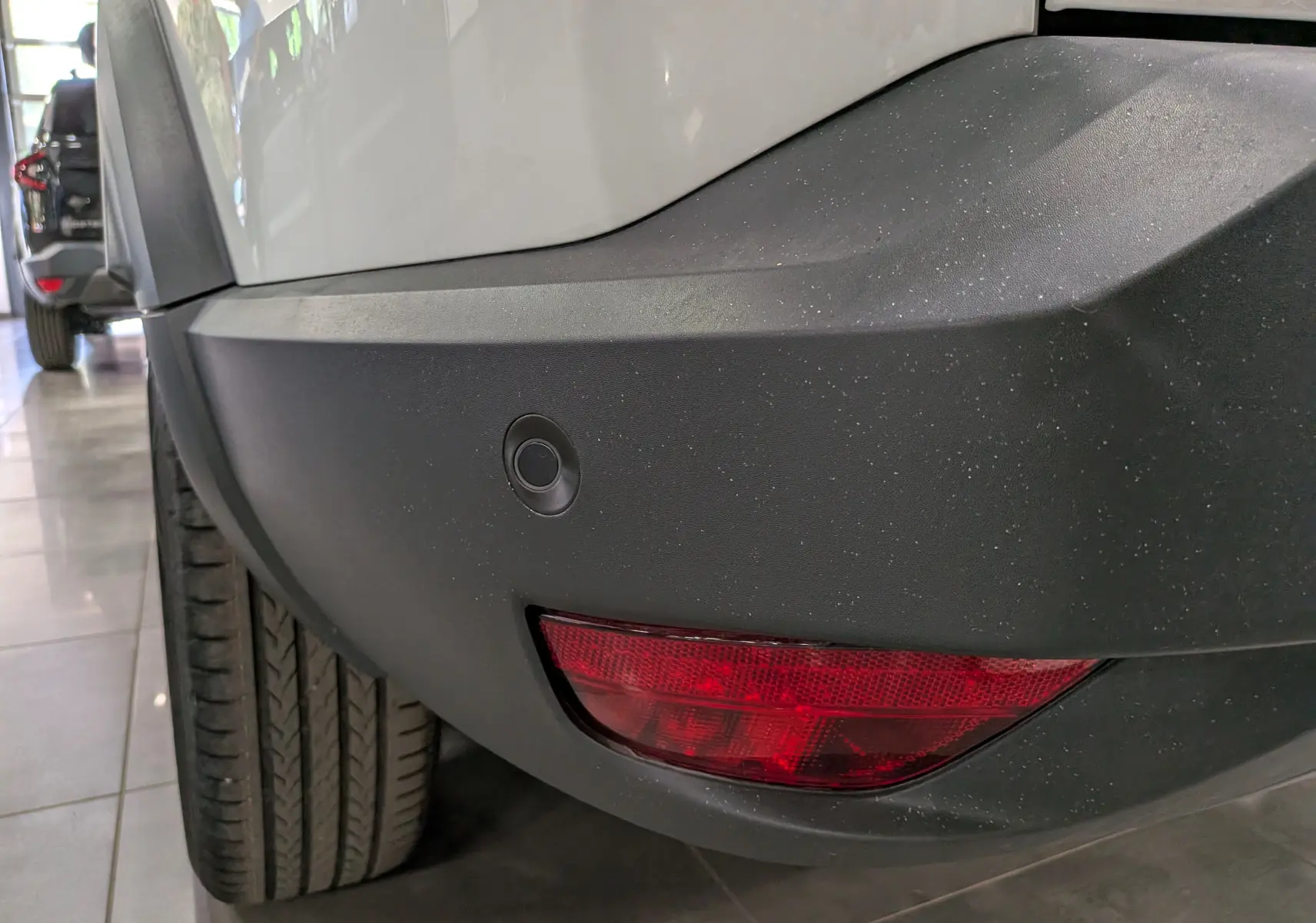 Gros plan sur le pare-chocs arrière droit noir et feu rouge du Dacia Bigster blanc glacier, avec capteur de recul visible.