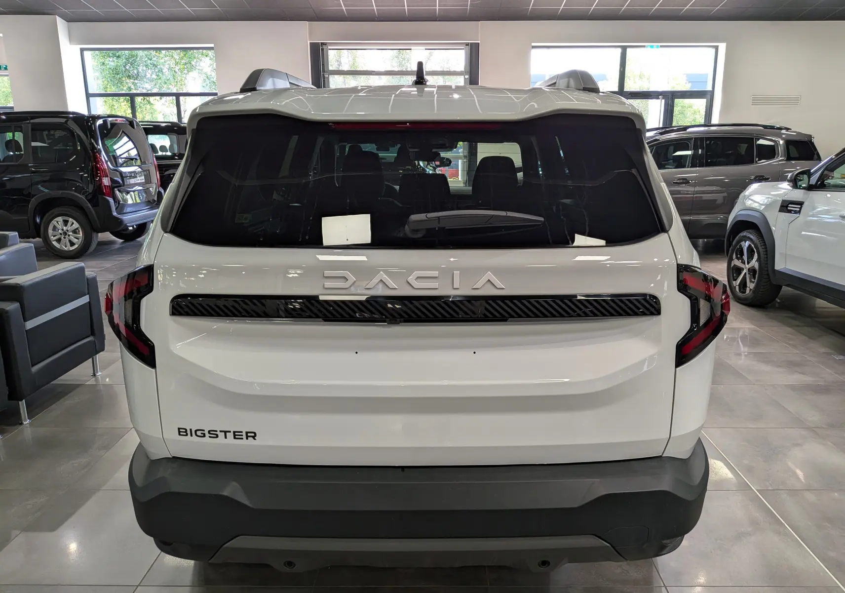 Vue arrière d'un Dacia Bigster blanc Glacier en showroom, avec logo DACIA et feux arrière noirs distinctifs.