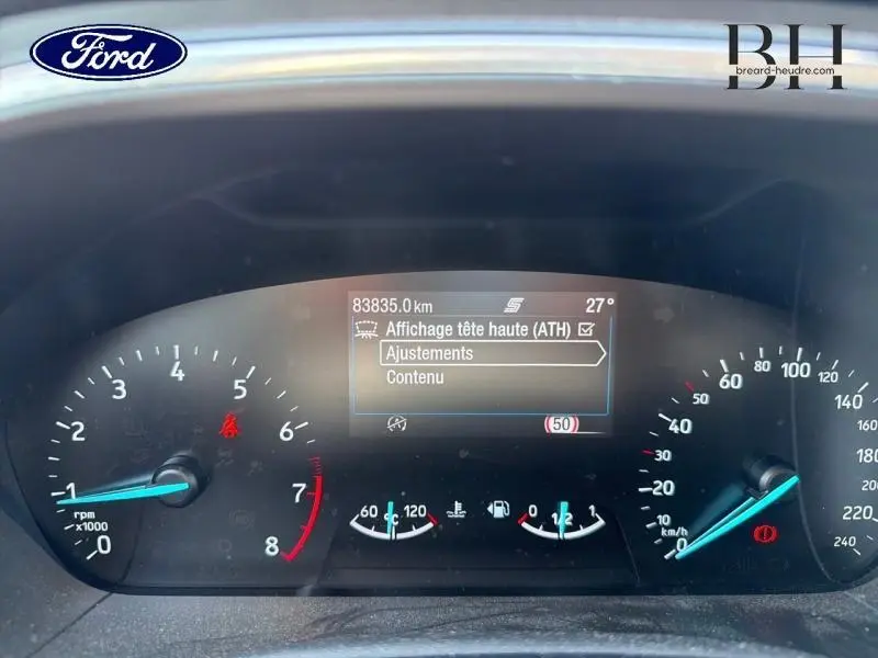 Tableau de bord numérique de Ford Focus noir, affichant les compteurs et menu tête haute, vue frontale rapprochée.