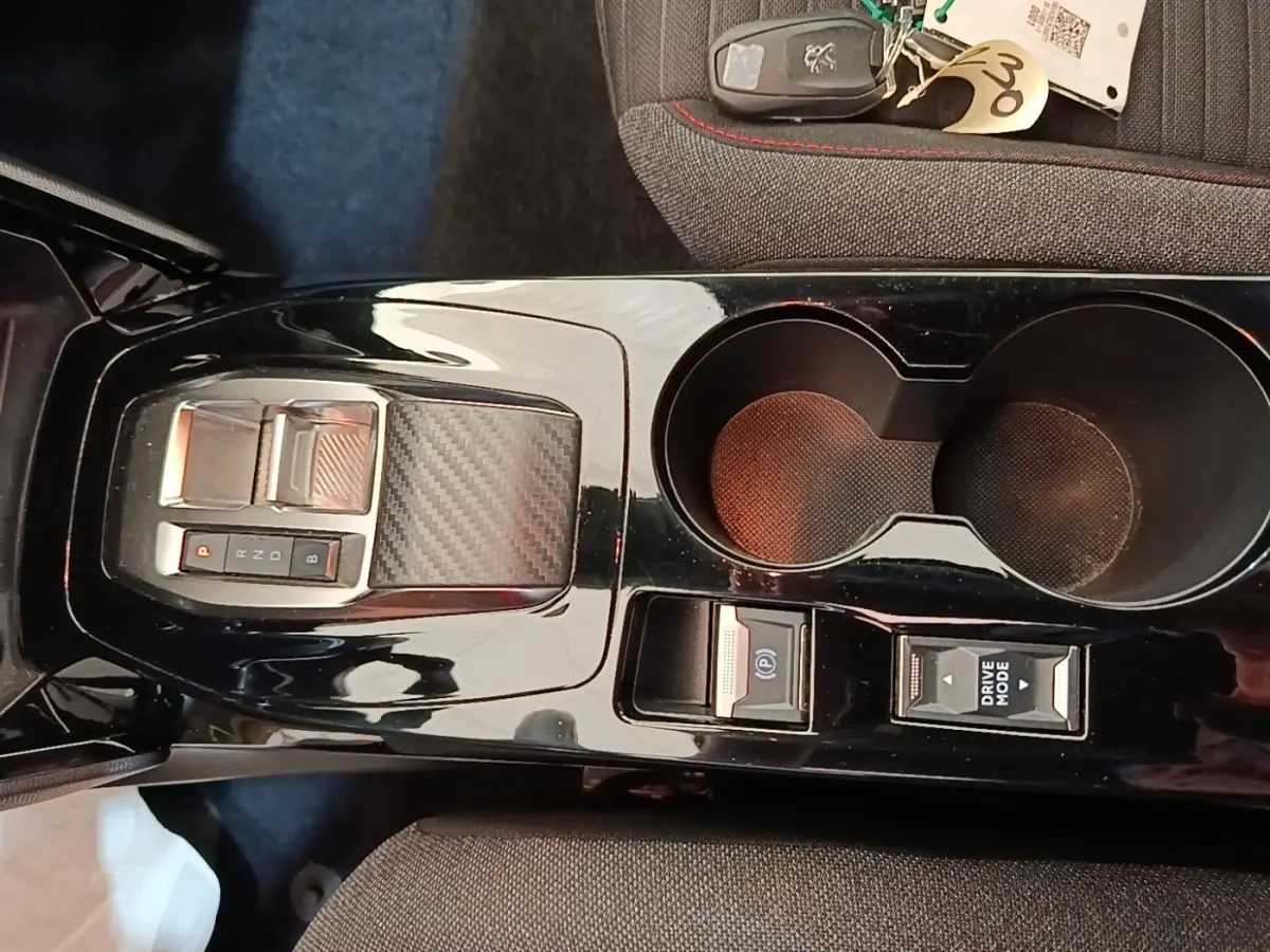 Vue rapprochée de la console centrale noire brillante du Peugeot E-2008 électrique avec sélecteur de vitesse et porte-gobelets.