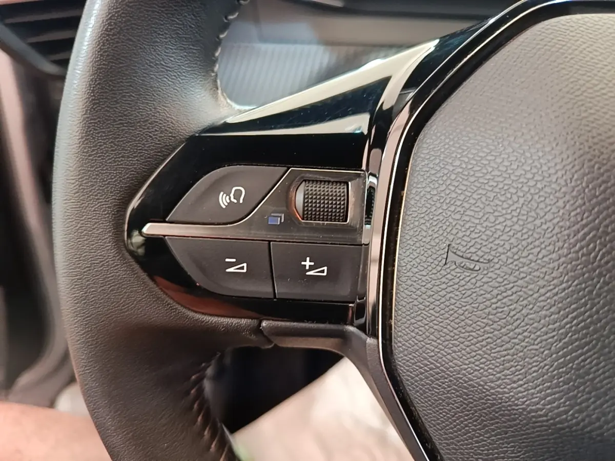 Gros plan sur le côté gauche du volant cuir multifonctions du Peugeot E-2008 électrique gris clair 2023.