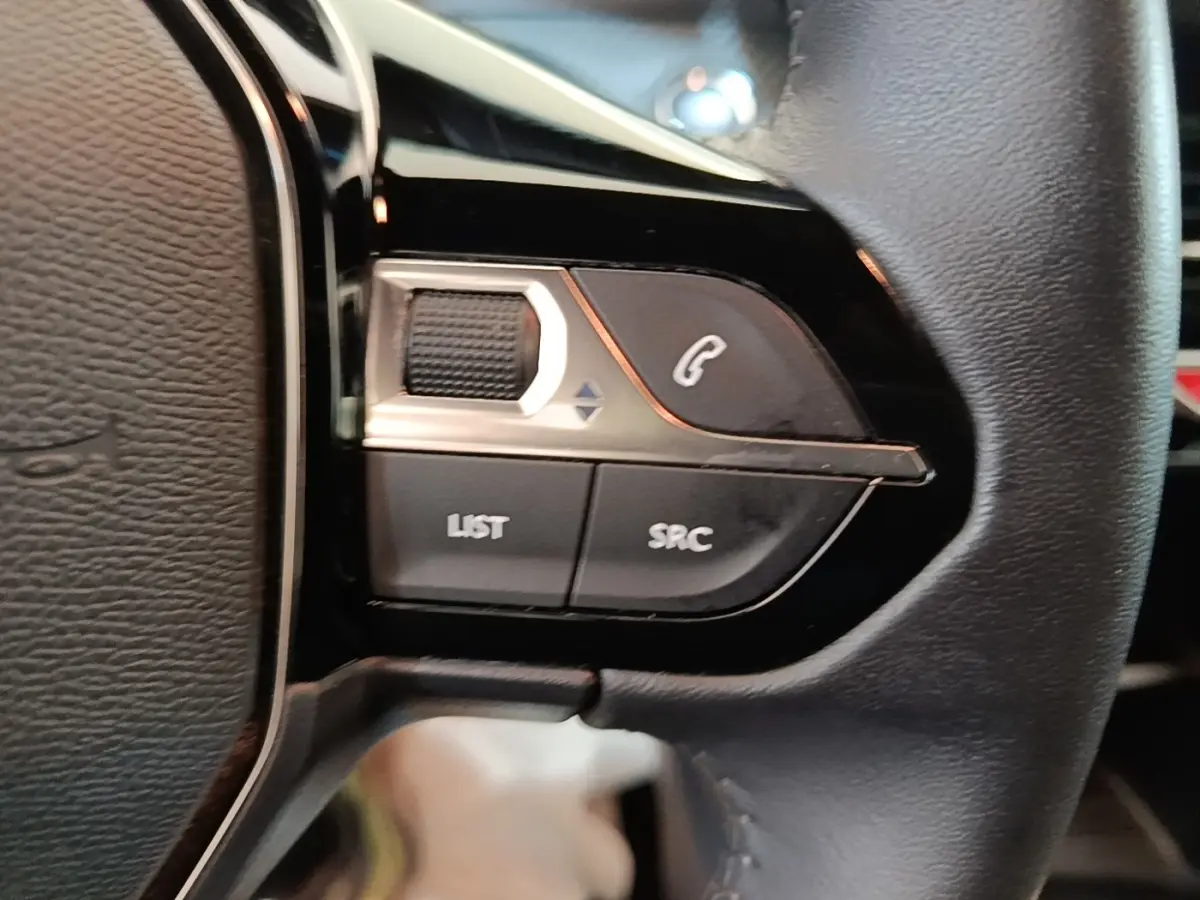Gros plan sur les commandes gauche du volant cuir multifonctions du Peugeot E-2008 électrique gris clair 2023.