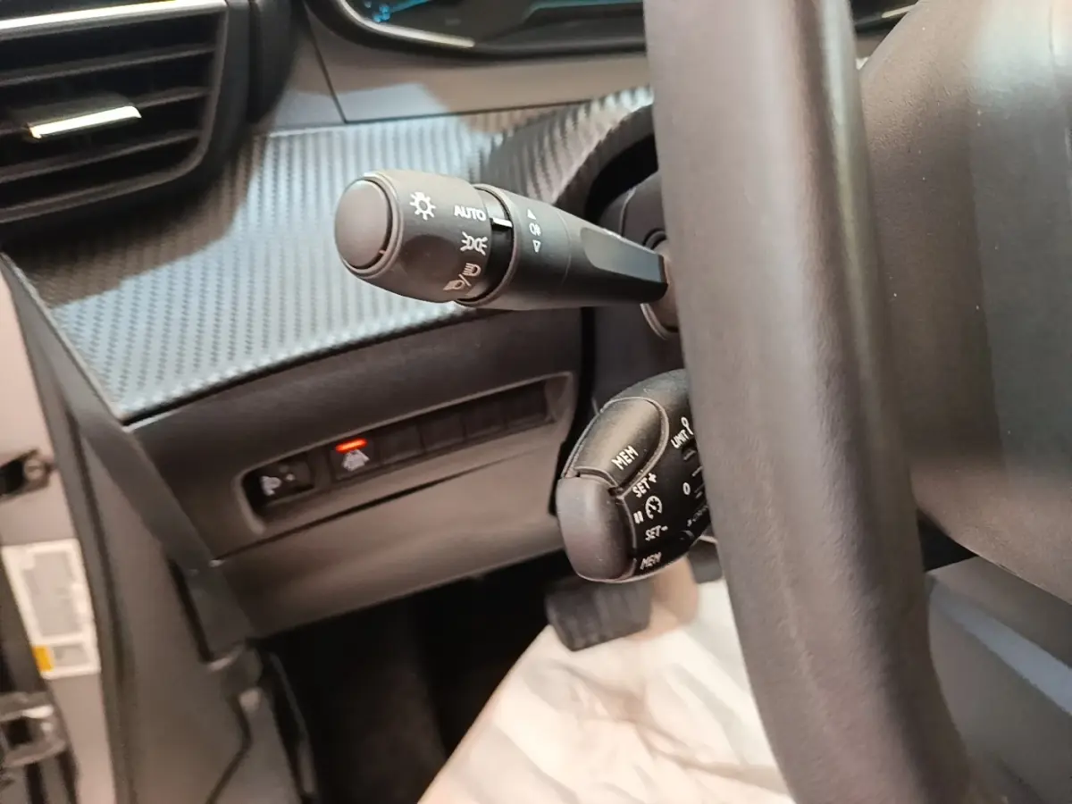 Gros plan sur la colonne de direction et commandes derrière volant cuir noir du Peugeot E-2008 électrique gris clair.