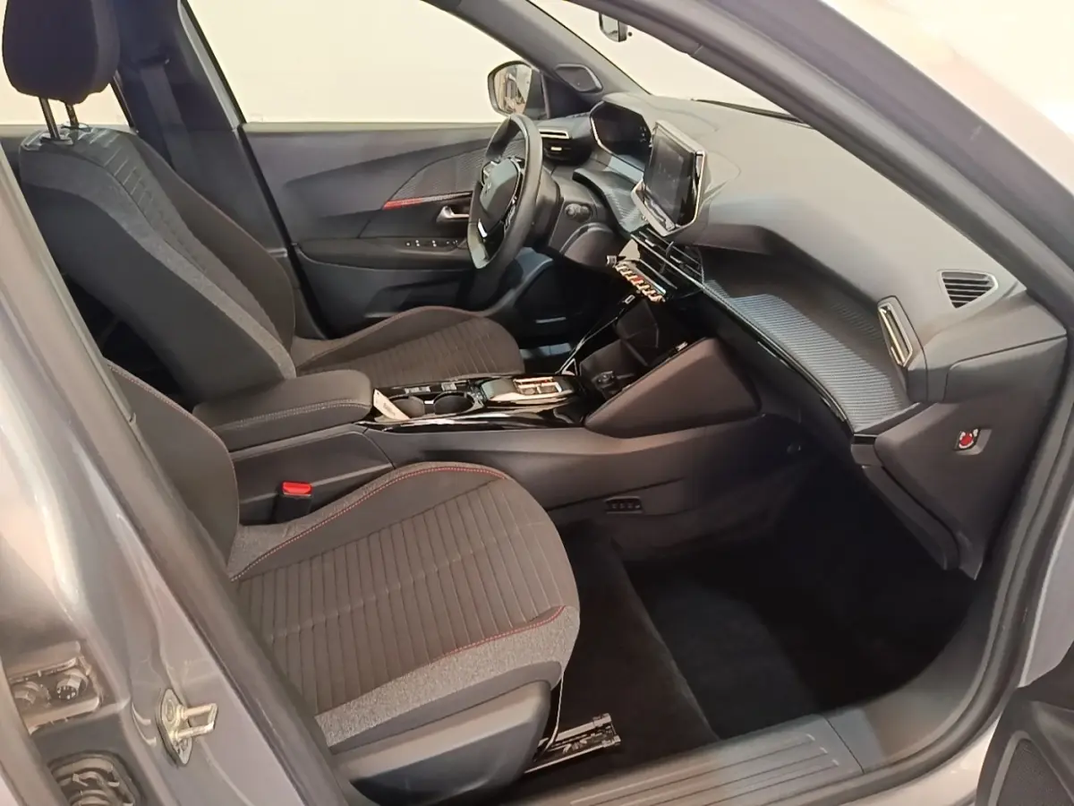Vue intérieure côté conducteur du Peugeot E-2008 électrique gris clair, avec tableau de bord moderne et sièges tissu noirs.