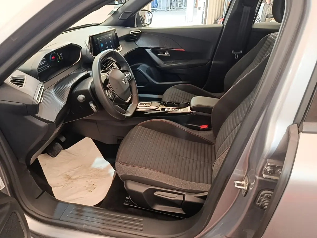 Vue intérieure côté conducteur du Peugeot E-2008 électrique gris clair 2023, avec volant cuir multifonctions et tableau de bord numérique.