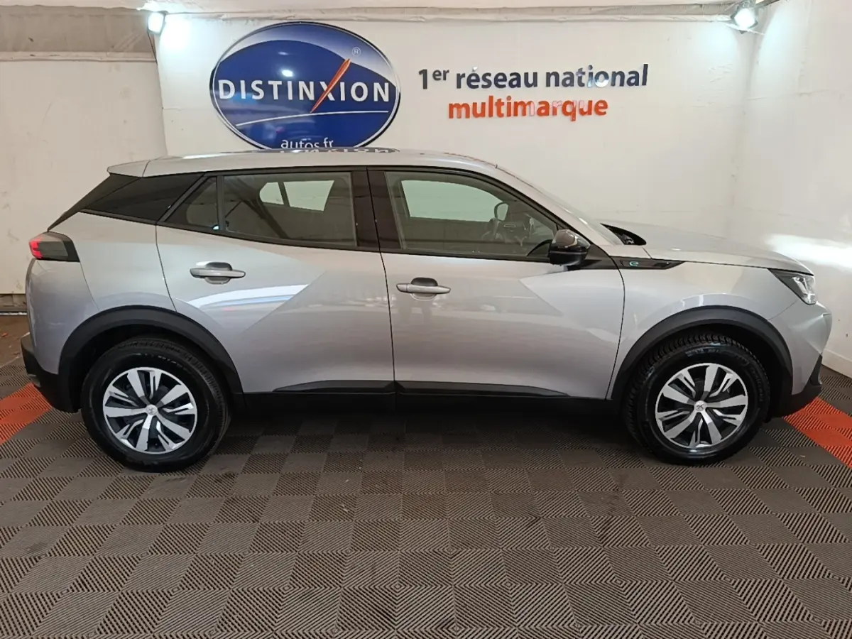 Peugeot E-2008 électrique gris clair en profil côté gauche, avec jantes alliage et toit noir contrasté.