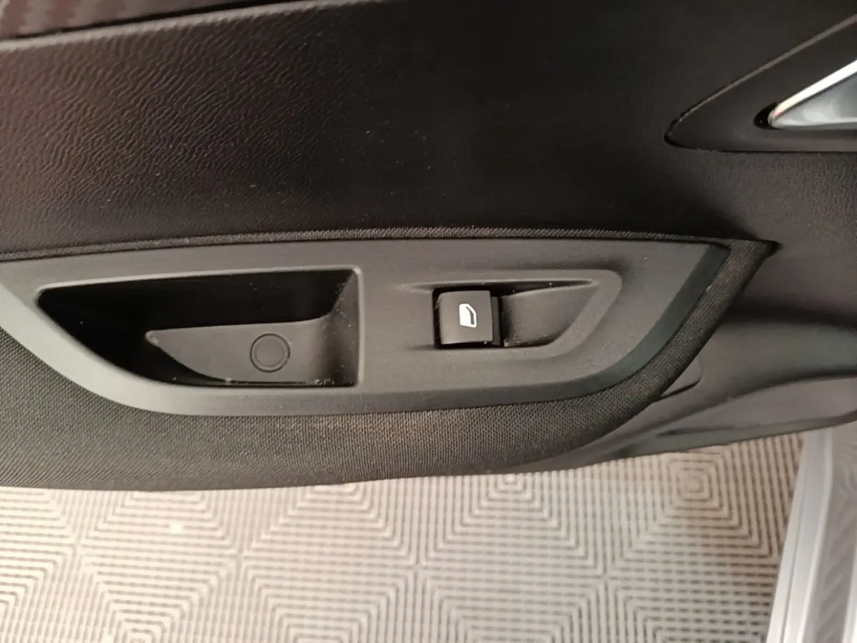 Gros plan sur la commande de lève-vitre côté porte intérieure d’une Peugeot E-2008 électrique gris clair.