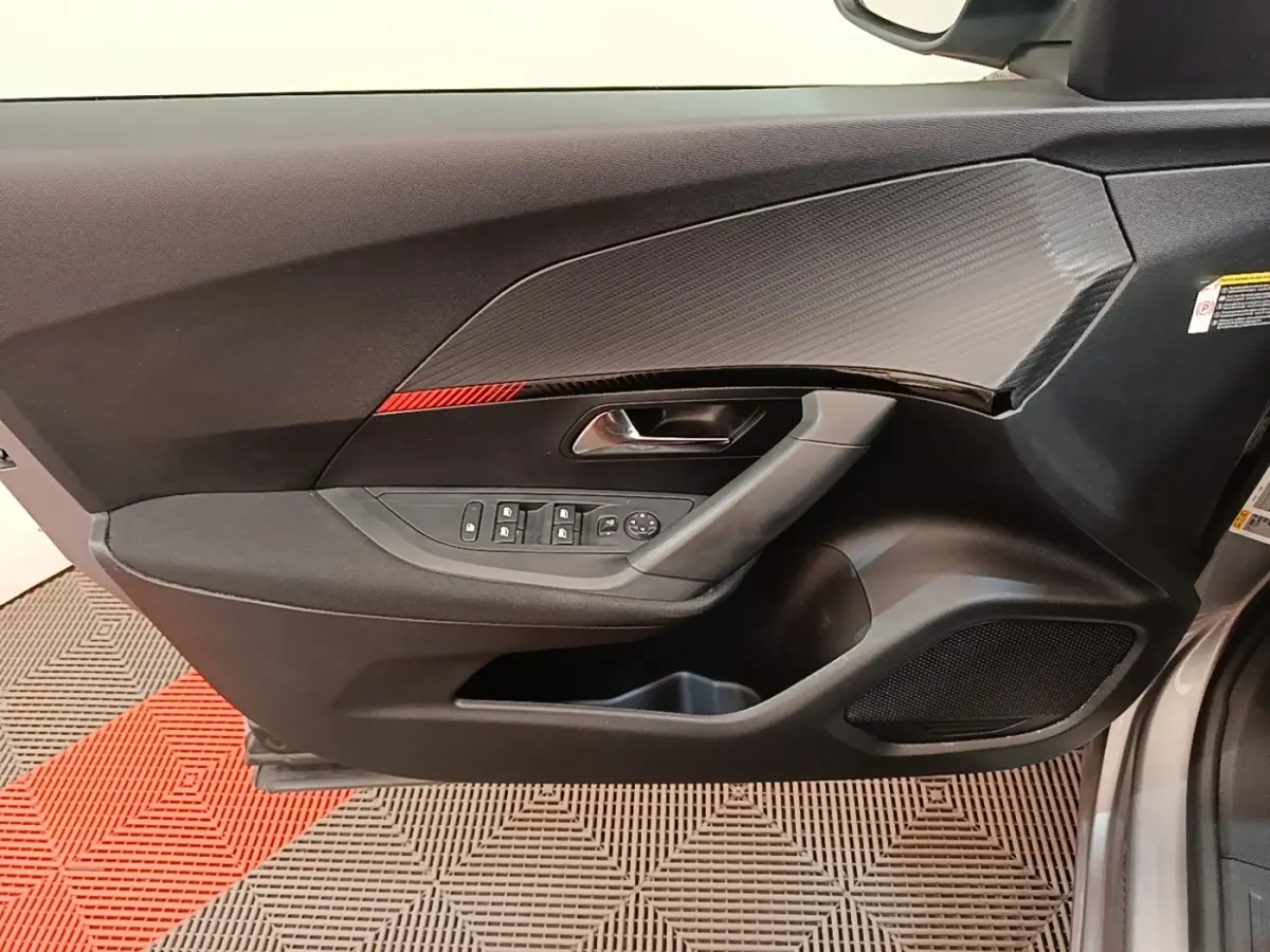 Vue intérieure côté gauche de la porte avant gris clair du Peugeot E-2008 électrique avec insert carbone et bande rouge décorative.