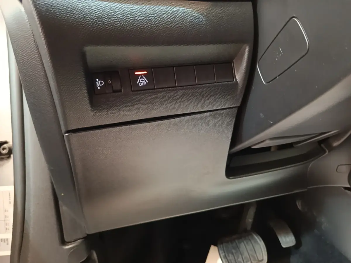 Vue intérieure côté gauche du tableau de bord gris foncé du Peugeot E-2008 électrique avec commandes d'assistance et pédales visibles.
