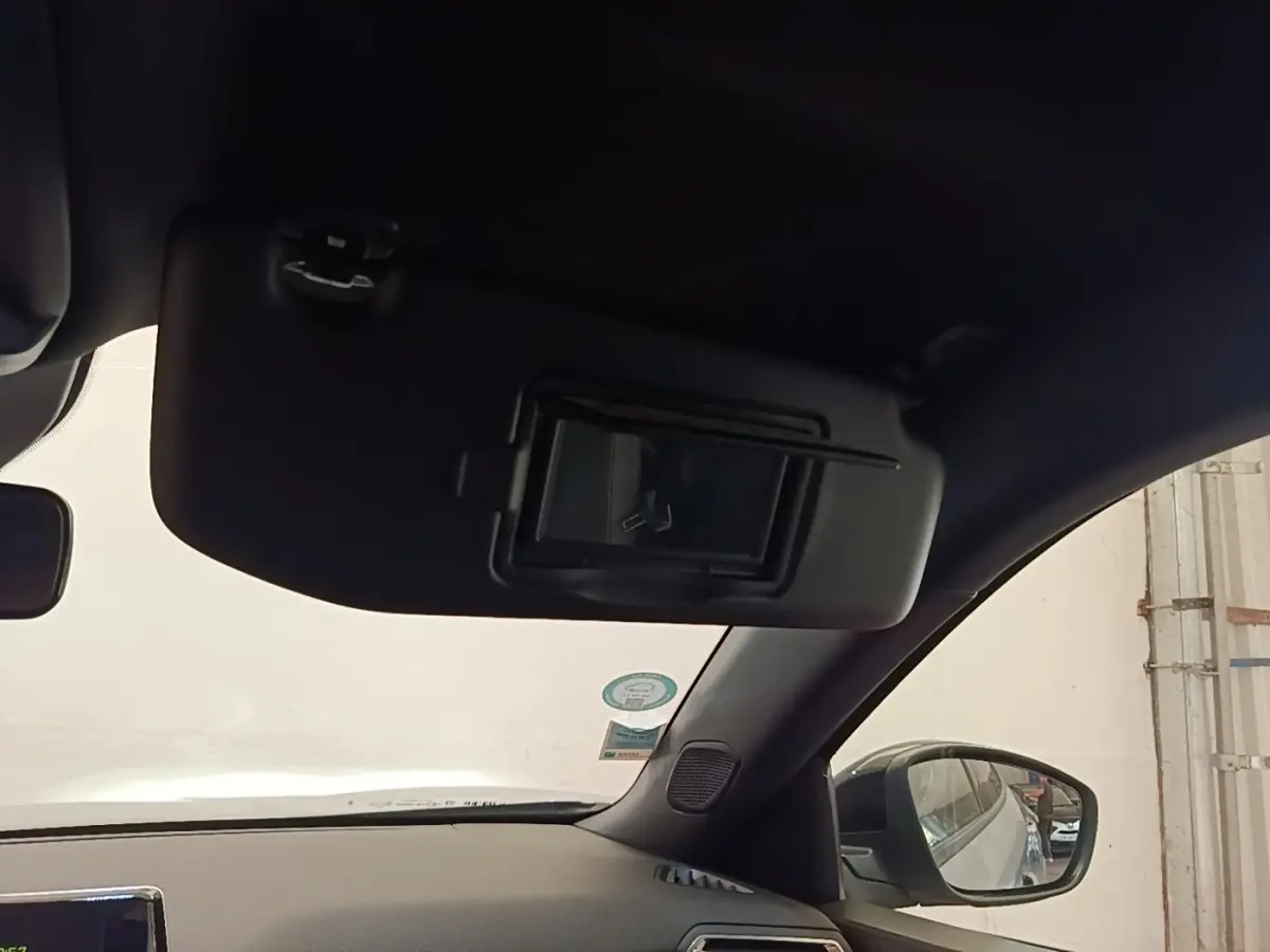 Vue intérieure côté passager du pare-soleil avec miroir, rétroviseur et partie du tableau de bord noir du Peugeot E-2008 gris clair.