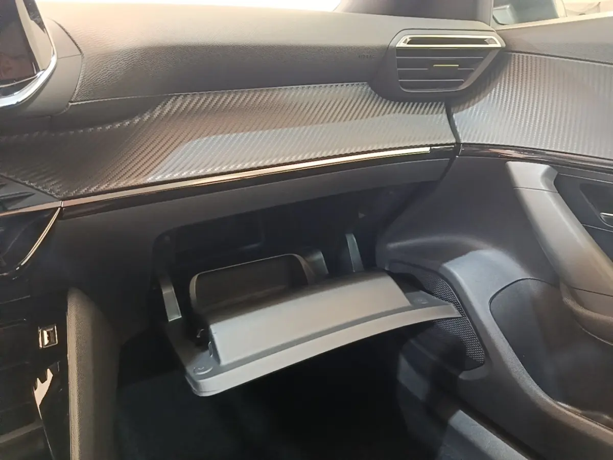 Vue intérieure côté passager du tableau de bord gris foncé et boîte à gants ouverte du Peugeot E-2008 électrique 2023.