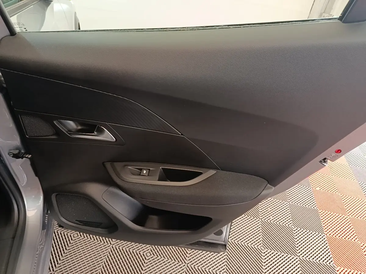 Vue intérieure de la porte côté gauche gris clair du Peugeot E-2008 électrique Active Pack 2023, avec commande de vitre.