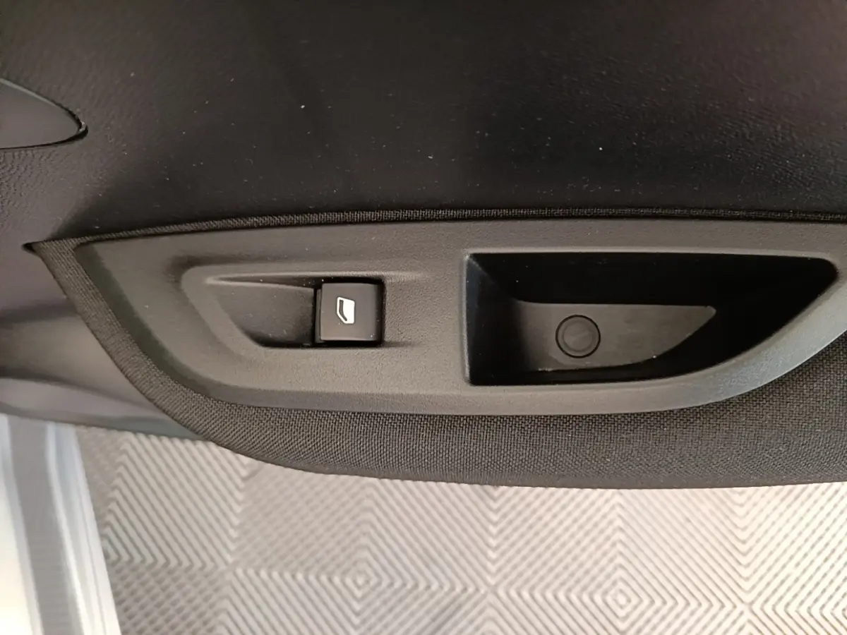 Détail du bouton d'ouverture de coffre sur le panneau intérieur noir d'un Peugeot E-2008 gris clair électrique.