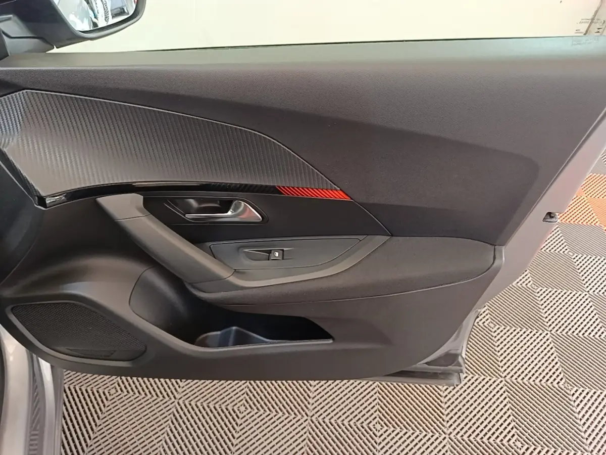 Intérieur côté gauche de la porte avant gris clair du Peugeot E-2008 électrique avec insert décoratif noir et rouge.