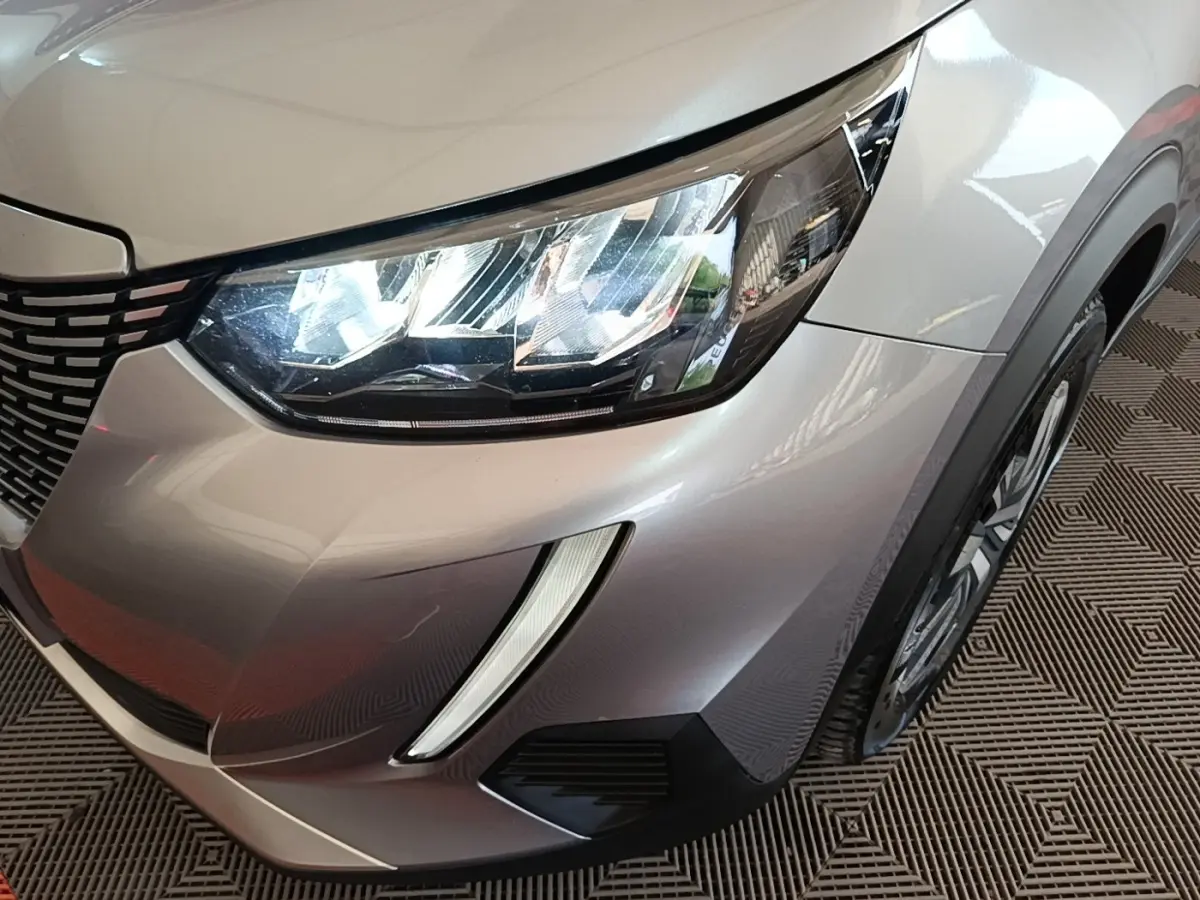 Gros plan sur l'avant droit gris clair du Peugeot E-2008 électrique avec phares LED et calandre distinctive.