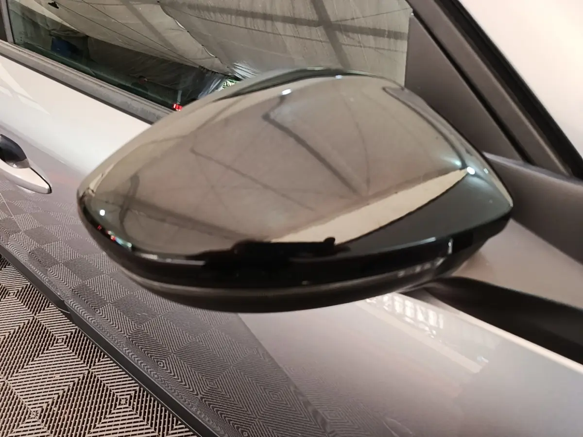 Rétroviseur noir brillant côté gauche d’un Peugeot E-2008 électrique gris clair, vue rapprochée en extérieur.