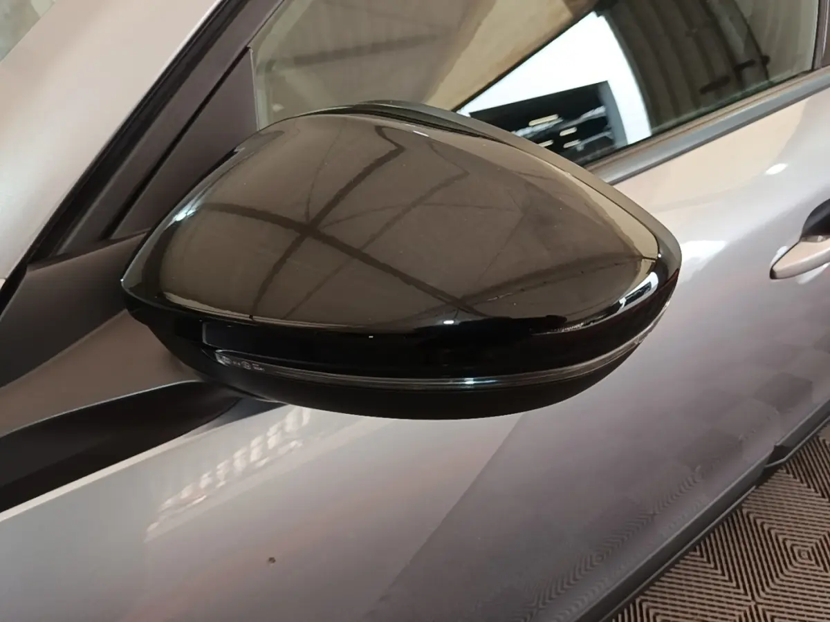 Rétroviseur noir en gros plan côté gauche d’un Peugeot E-2008 électrique gris clair, vue partielle du véhicule.