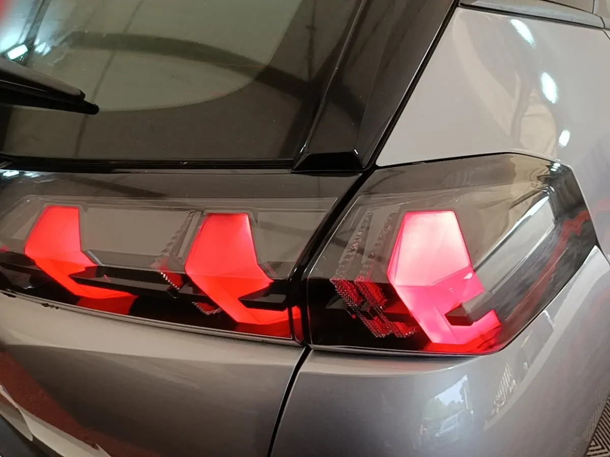 Gros plan sur les feux arrière rouges d’un Peugeot E-2008 électrique gris clair, vue côté droit arrière.