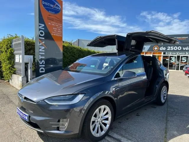 Tesla Model X gris en 3/4 avant droit avec portes papillon ouvertes sur un parking ensoleillé