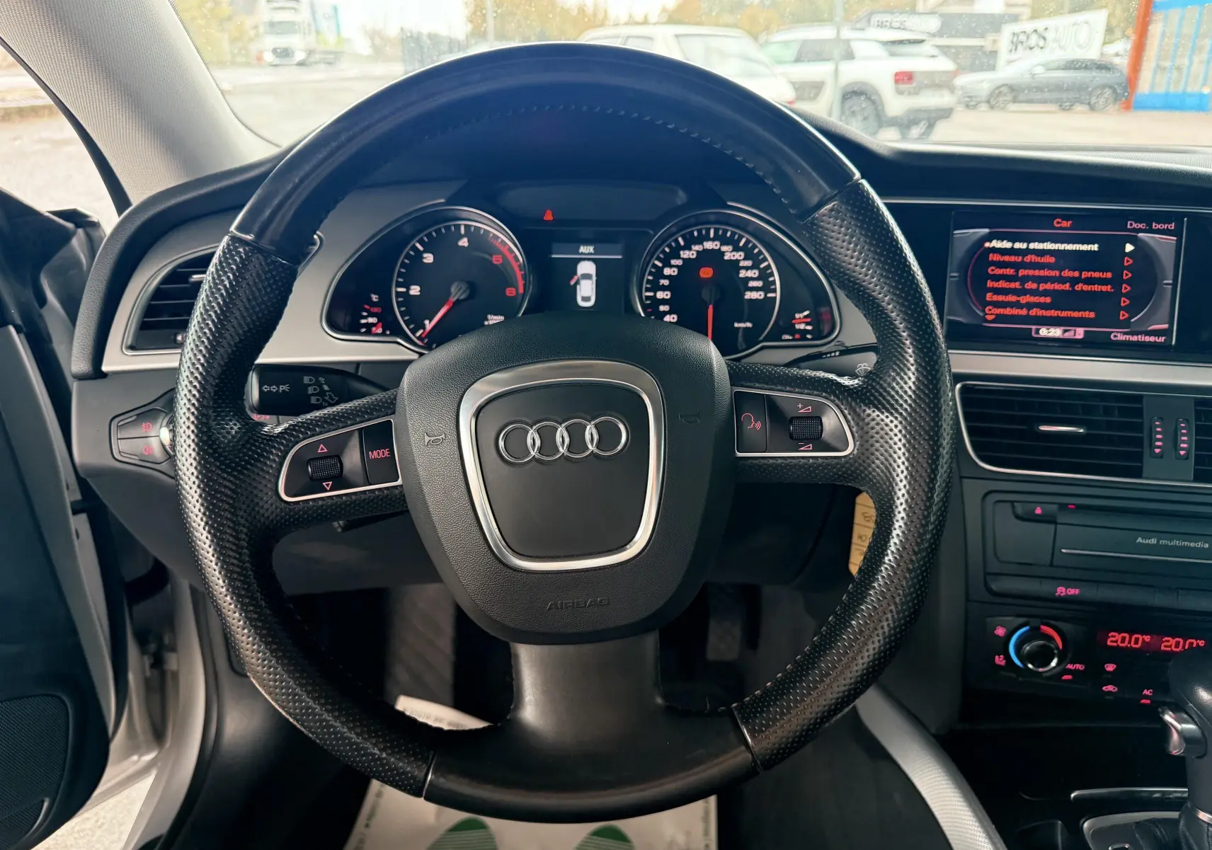 Vue rapprochée du volant en cuir noir d'une Audi A5 2011 avec tableau de bord et écran multimédia allumés.