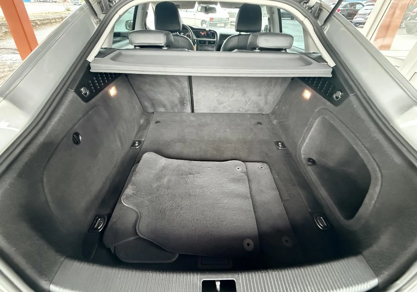 Coffre ouvert d'une Audi A5 Sportback gris, vue intérieure montrant tapis et banquette arrière en cuir noir.