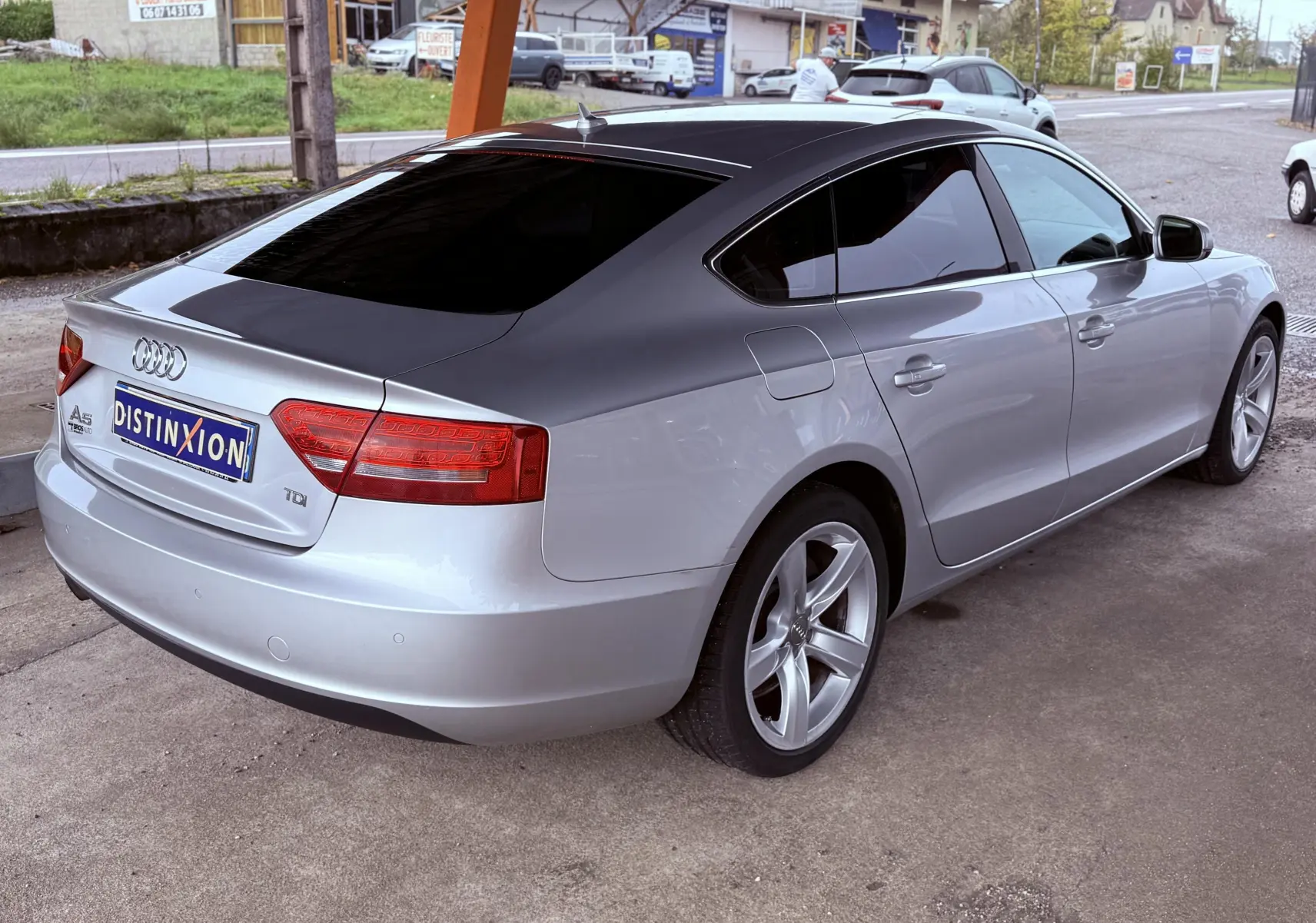 Audi A5 gris vue 3/4 arrière droit, toit noir et jantes alliage 5 branches, stationnée sur parking extérieur.