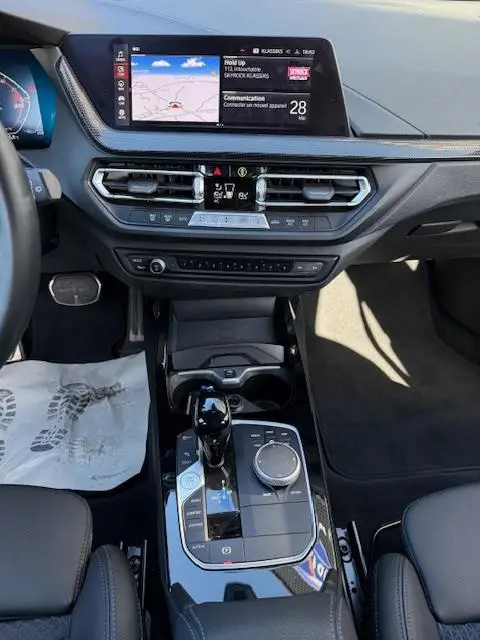 Vue intérieure centrée sur la console centrale et tableau de bord de la BMW Série 1 118d Edition Sport gris foncé avec écran tactile et molette de sélection.