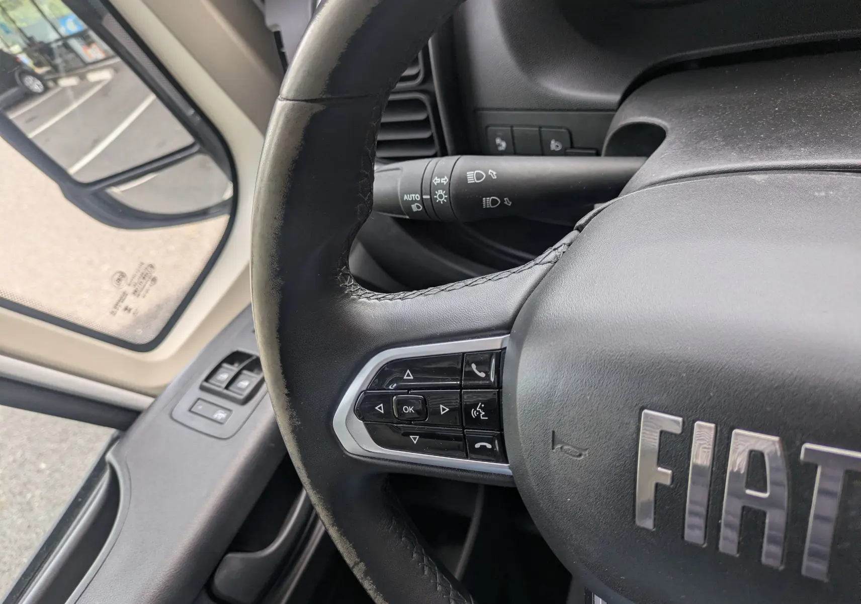 Gros plan sur le volant noir du Fiat Ducato Fourgon 2025 avec commandes intégrées côté gauche et rétroviseur extérieur visible.