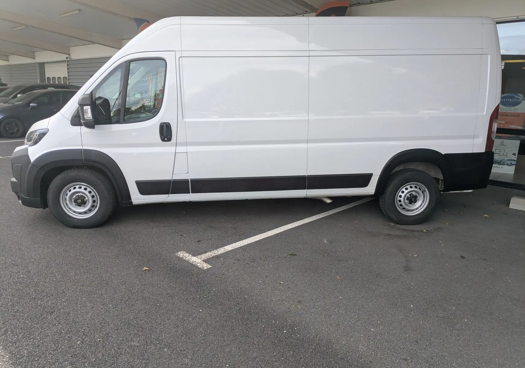 Fiat Ducato Fourgon blanc vu de profil côté gauche, stationné sous un abri avec détails noirs sur les bas de caisse.