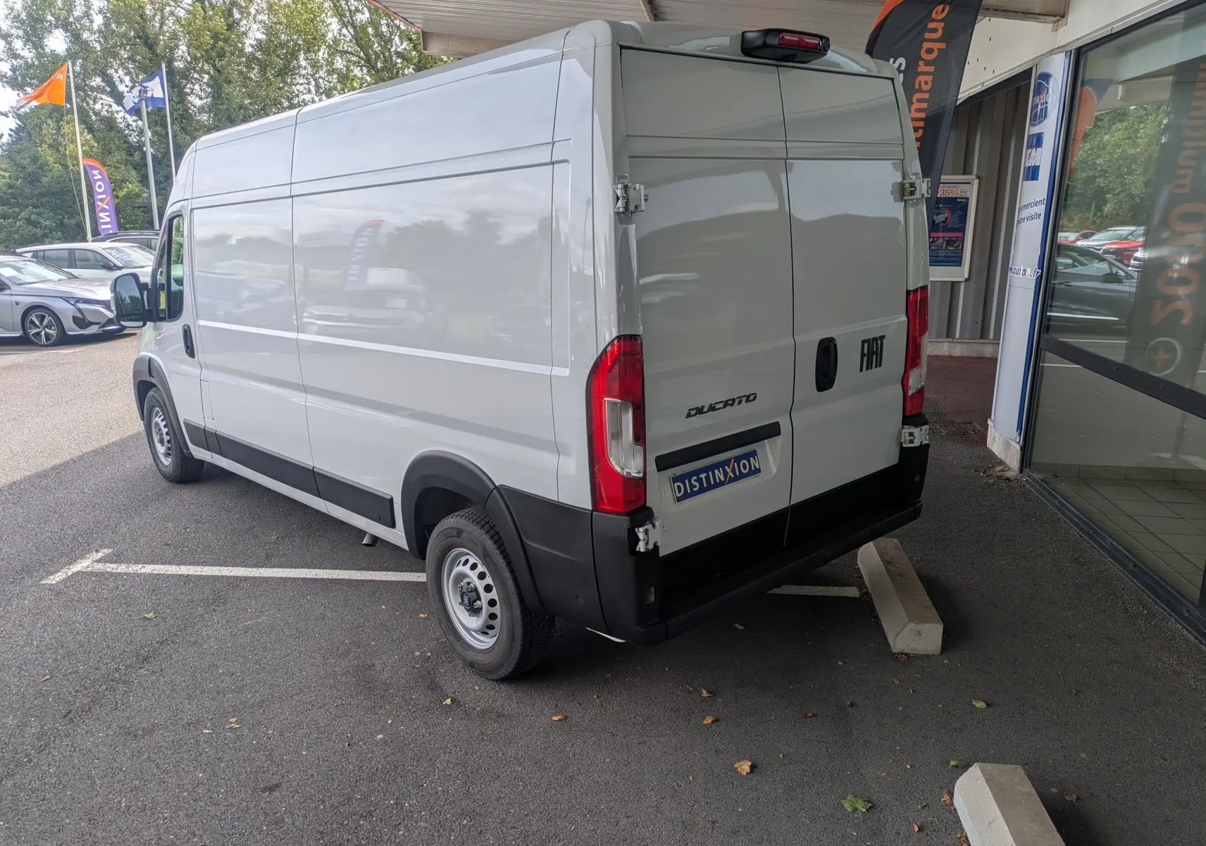 Fiat Ducato Fourgon blanc en vue 3/4 arrière droit, stationné devant un bâtiment avec portes arrière fermées.