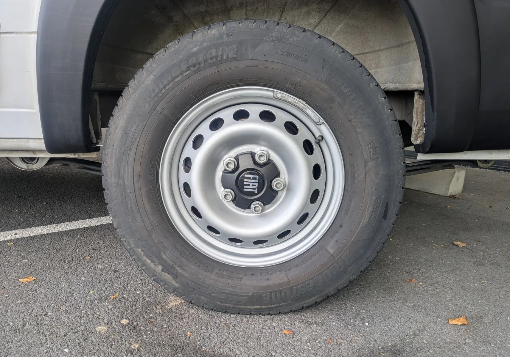 Gros plan sur la roue avant droite d’un FIAT Ducato Fourgon blanc avec jante acier et logo FIAT au centre.