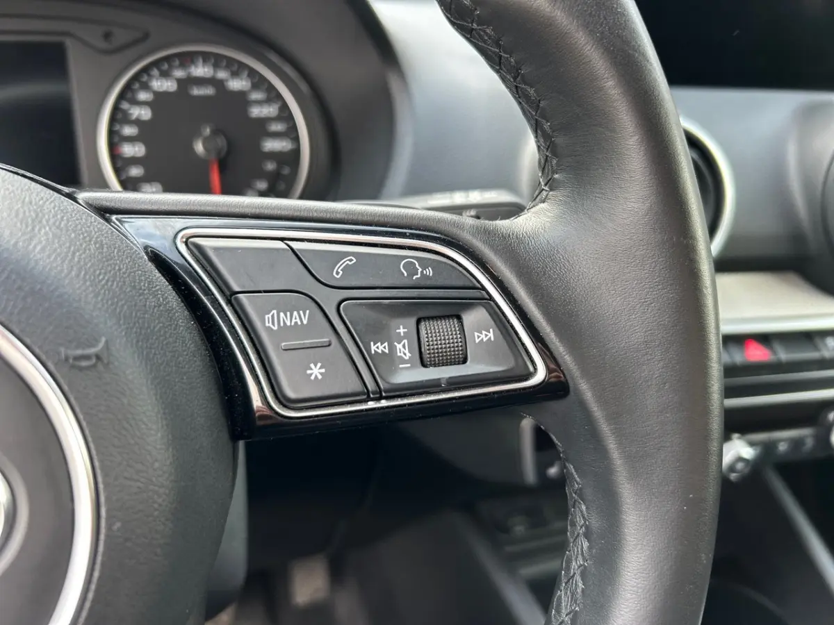 Gros plan sur les commandes gauche du volant cuir noir de l'Audi Q2 35 TFSI 2023 avec tableau de bord en arrière-plan.