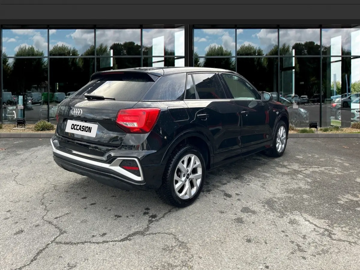 Audi Q2 noir vue 3/4 arrière droit, avec jantes argentées et feux arrière rouges, stationné devant une vitrine.