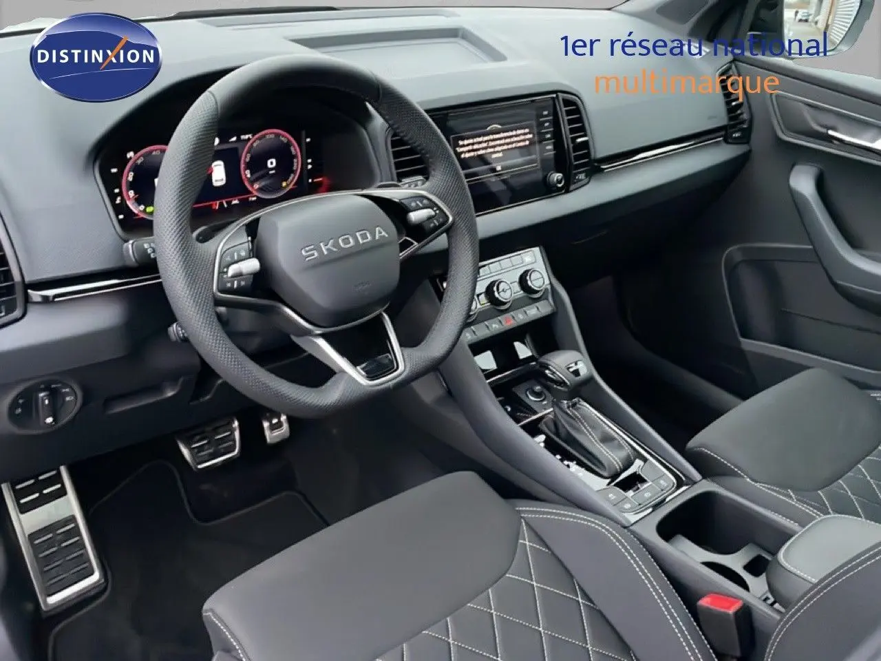 Intérieur de la Skoda Karoq 2025 vu côté conducteur, avec volant cuir, tableau de bord numérique et sièges tissu noir à surpiqûres.