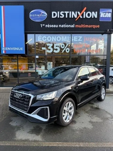 Audi Q2 noir vue 3/4 avant droit, garée devant une concession Distinxion avec reflets sur la carrosserie.