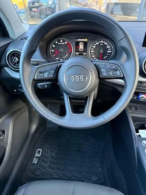 Vue intérieure centrée sur le volant cuir multifonctions d’un Audi Q2 noir 2023 avec tableau de bord digital.