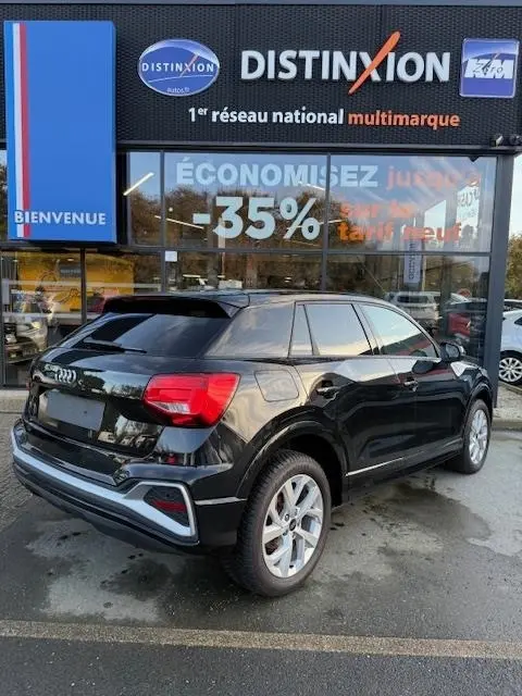 Audi Q2 noir vue 3/4 arrière droit, stationné devant une vitrine avec enseigne Distinxion.