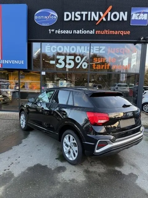 Audi Q2 noir vue 3/4 arrière droit, stationné devant une vitrine avec enseigne Distinxion.