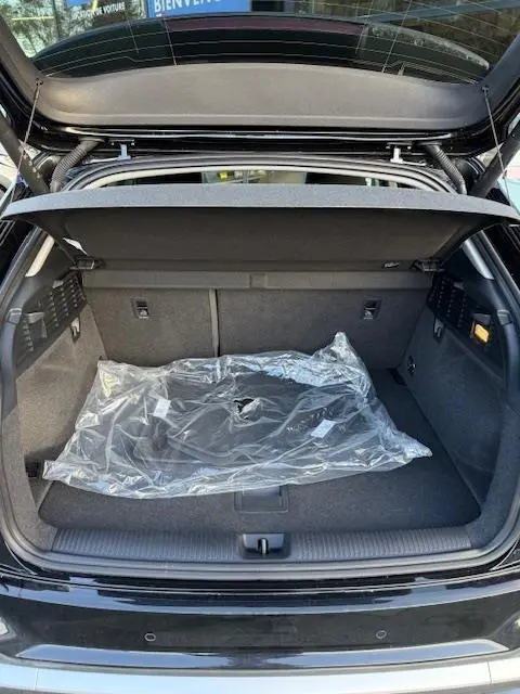 Coffre ouvert vu de l'arrière d'un Audi Q2 noir 2023, avec tapis de sol protégé sous plastique visible.