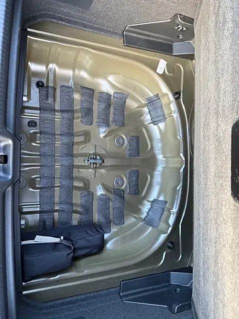 Vue plongeante sur le compartiment de roue de secours vide de l'Audi Q2 35 TFSI 150 S Line noir, montrant la structure métallique.