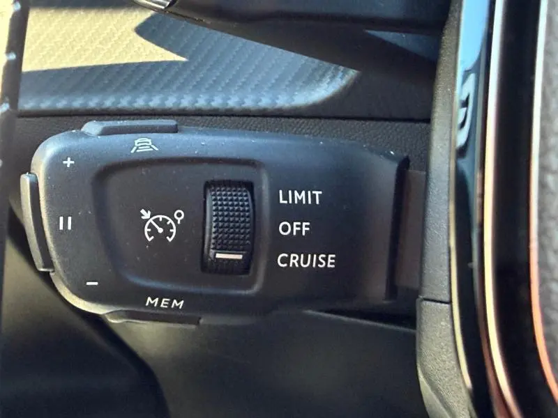 Gros plan sur la commande de régulateur de vitesse à gauche du volant dans un Peugeot 2008 gris 2024.