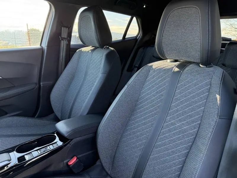 Vue intérieure rapprochée des sièges avant en tissu gris embossé du Peugeot 2008 2024, avec accoudoir central et porte-gobelets.