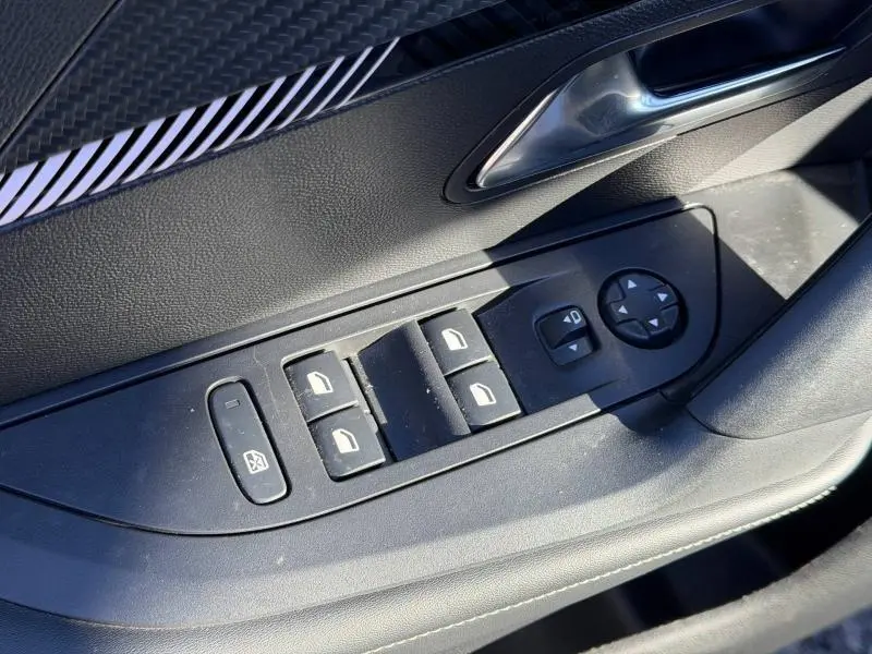 Vue rapprochée de la commande des vitres côté conducteur dans une Peugeot 2008 gris, avec boutons noirs et poignée argentée.