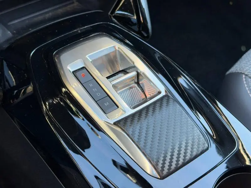 Gros plan sur la console centrale noire brillante avec levier de vitesses automatique et insert effet carbone dans une Peugeot 2008 gris Selenium.
