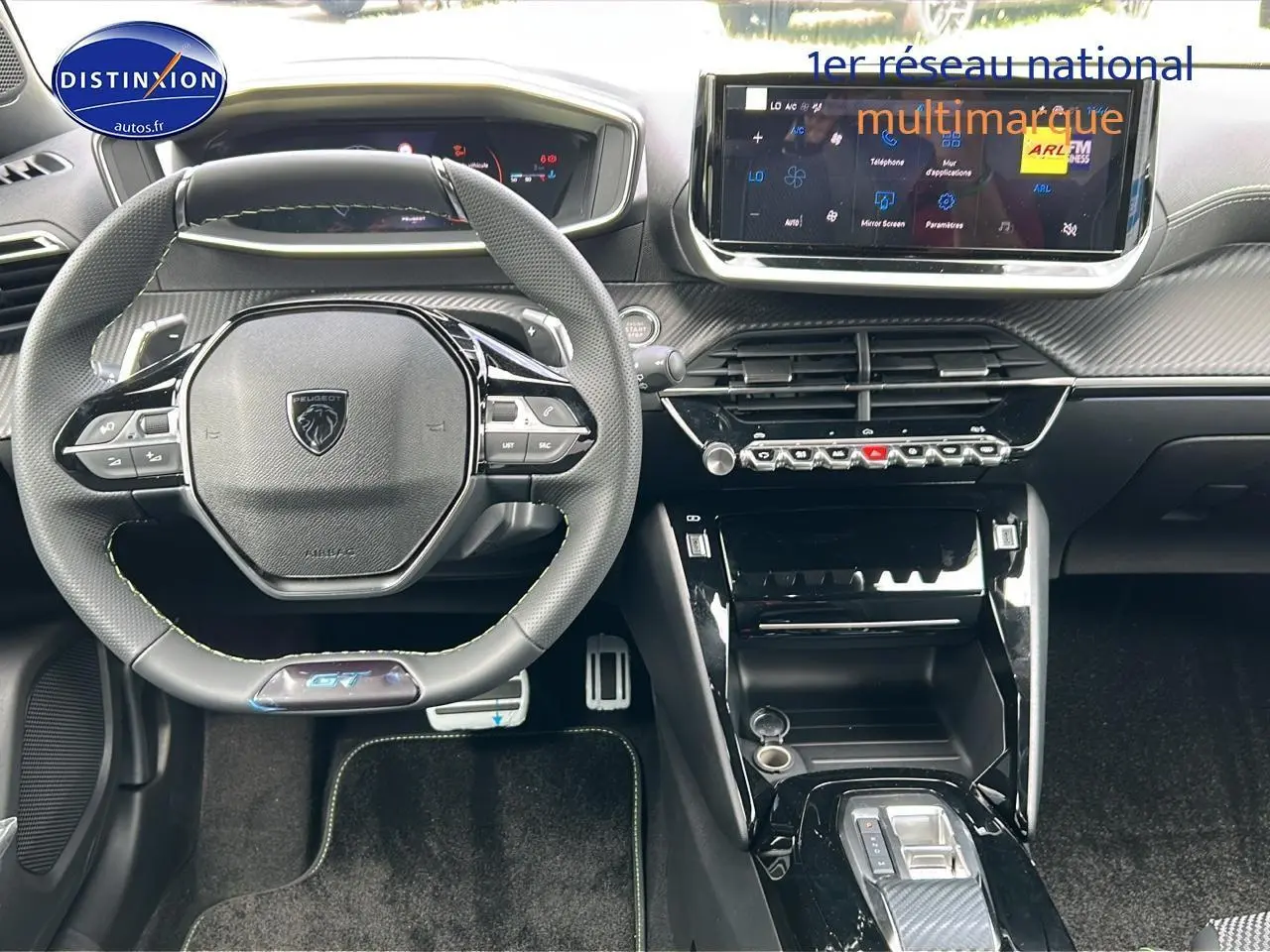 Vue intérieure frontale du tableau de bord et volant cuir noir avec logo Peugeot GT, écran tactile et console centrale moderne.
