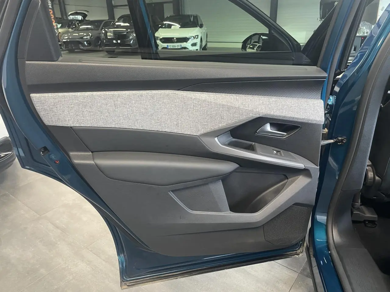 Vue intérieure de la porte arrière gauche bleu Obsession du Peugeot 5008 2025 avec habillage tissu gris et noir.