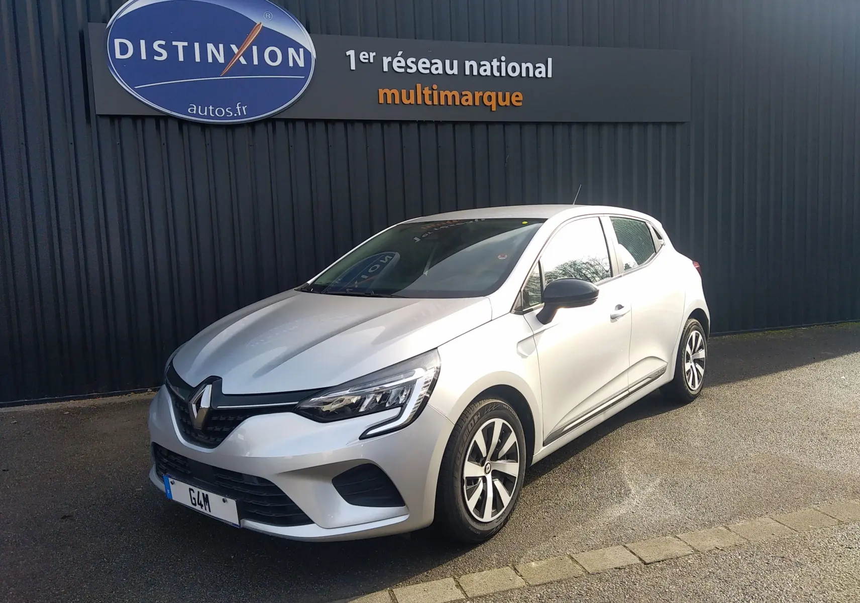 Renault Clio V gris en 3/4 avant droit, avec phares LED et jantes alliage, stationnée devant un mur noir.