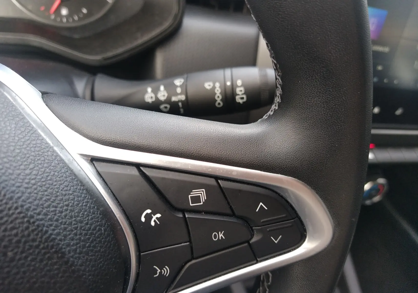 Gros plan sur les commandes multifonctions noires du volant en cuir d’une Renault Clio V gris, intérieur moderne.